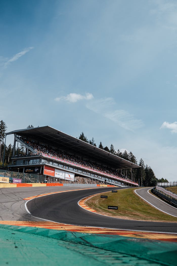 Dramatic view of a curving race track with a filled grandstand under a clear sky.